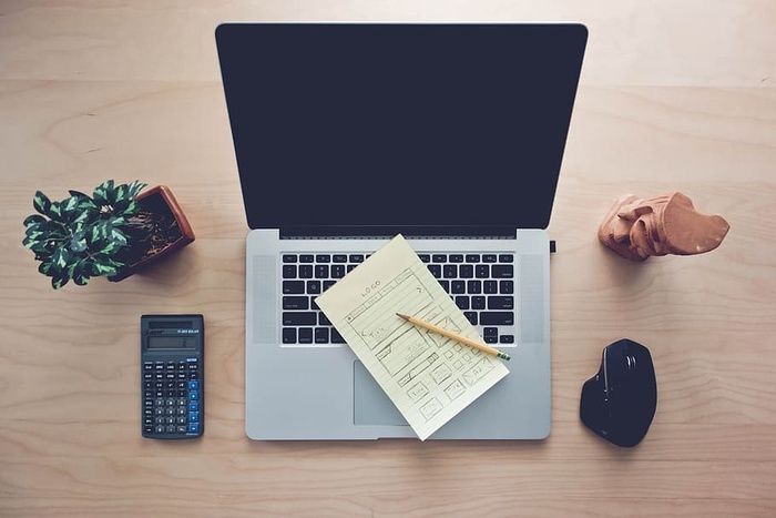 家庭办公桌设置的高角度视图，带有MacBook、计算器室内办公桌设备和带有木制迷你雕像的无线鼠标。