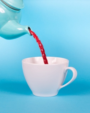 绿色茶壶将红色液体倒入白色茶杯特写摄影