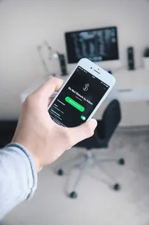 手持iPhone展示Spotify应用程序的人 手持iPhone展示Spotify应用程序的人