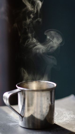 棕色表面上装满热液体的灰色不锈钢杯