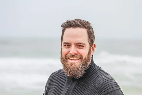 海滩附近穿着黑色拉链夹克的男子对着照片微笑 海滩附近穿着黑色拉链夹克的男子对着照片微笑