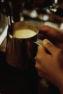 在分配器附近拿着装有牛奶的不锈钢杯子的人的选择性聚焦摄影