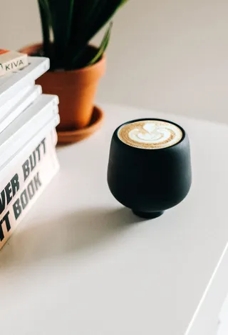 书籍旁的黑色陶瓷茶杯和白色木桌上的盆栽绿色植物