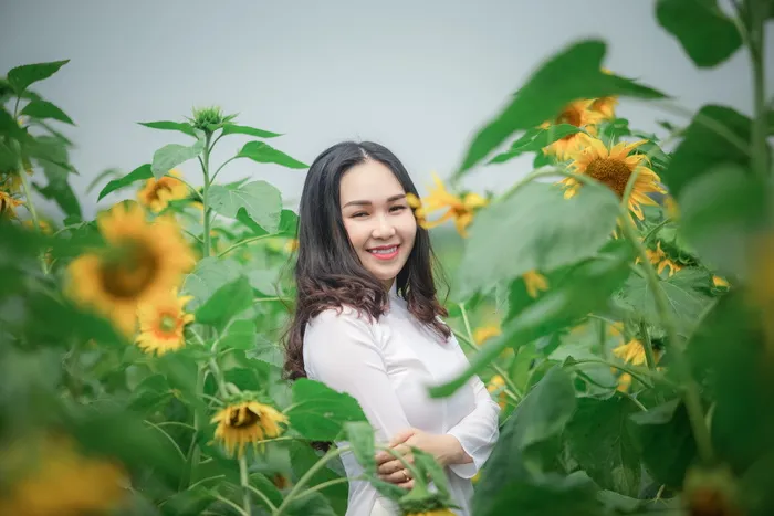 身穿白色衬衫的女子微笑着站在向日葵田附近