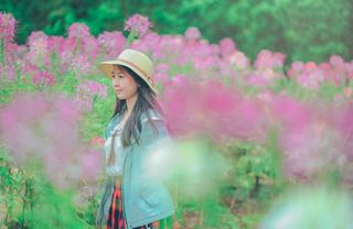 戴着太阳帽和蓝色夹克的女人站在鲜花的包围下