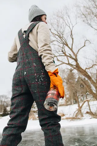 身穿米色毛衣的女子在无叶的树旁拿着瓶子