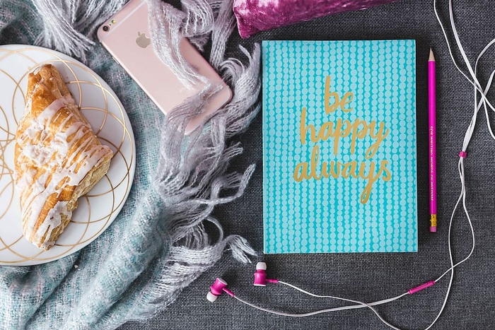 蓝色笔记本，带粉色iPhone、耳机和甜面包