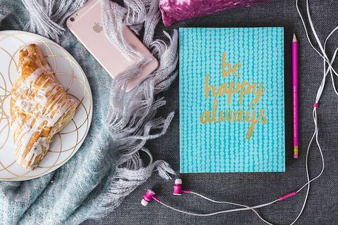 蓝色笔记本，带粉色iPhone、耳机和甜面包