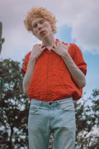 身穿橙色衬衫和蓝色牛仔牛仔裤的白化病男子站着的照片