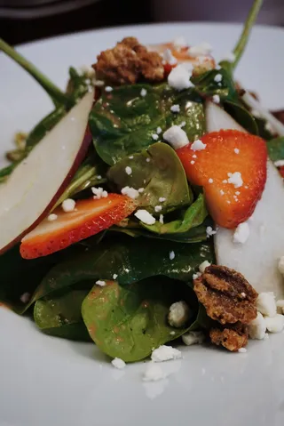 将草莓和绿叶蔬菜切片放在白色陶瓷盘上