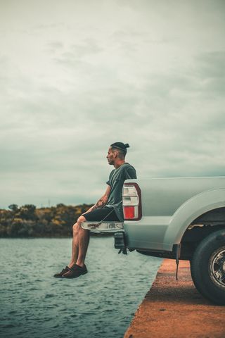 坐在靠近水体的汽车尾门上的男子