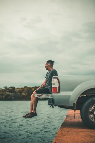 坐在靠近水体的汽车尾门上的男子