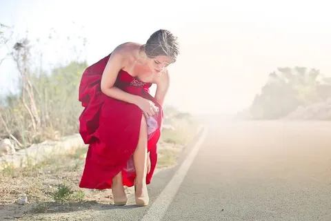 年轻成年女子穿着红色派对礼服,在拍照时调整鞋子 年轻成年女子穿着红色派对礼服,在拍照时调整鞋子