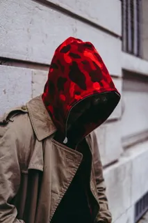 身穿米色夹克、头戴红色风帽的男子靠在墙上