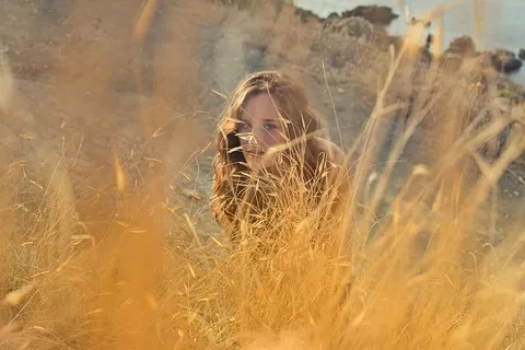 一位年轻的金发女郎在黄色草地后面的草地上摆姿势