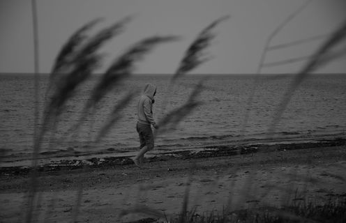 灰度照片，人物，连帽衫，走路，海边，忧郁，沮丧，气馁