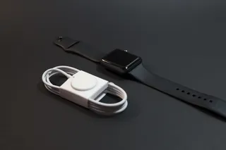 黑色铝制表壳苹果手表，磁性充电器旁边有运动表带