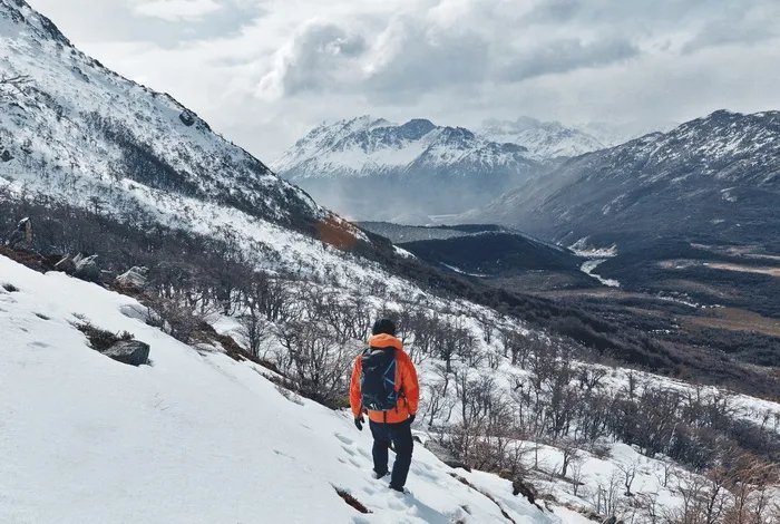 白天，穿着橙色夹克和黑色裤子的人在白雪覆盖的田野上行走