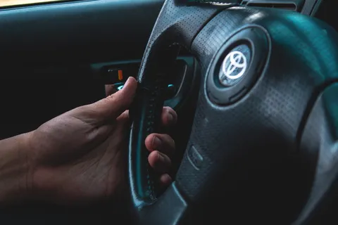 手持黑色丰田汽车方向盘的人