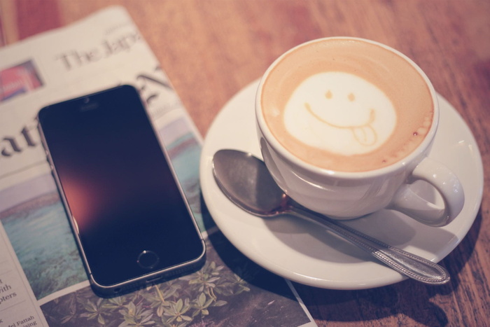 太空灰iPhone 5s旁边的白色陶瓷茶杯，配拿铁咖啡