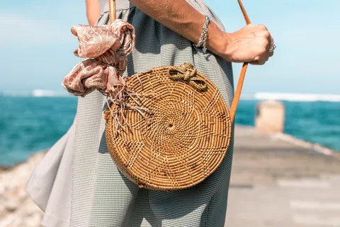 一名穿着灰色裙子和棕色藤条横挎包的妇女站在靠近水体的木质码头上 一名穿着灰色裙子和棕色藤条横挎包的妇女站在靠近水体的木质码头上
