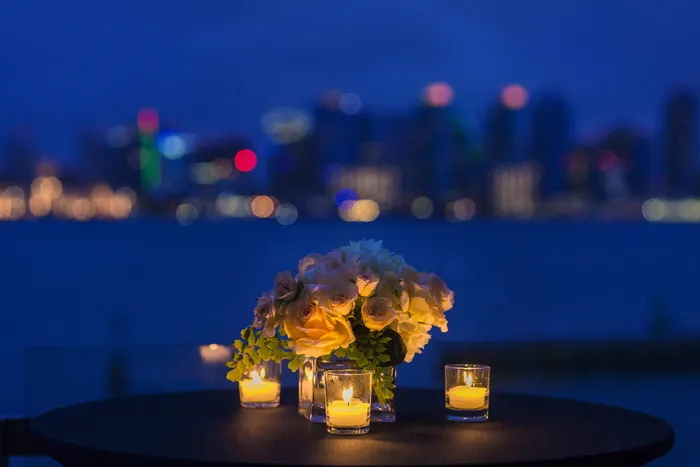 花瓶里的白玫瑰花束，棕色圆木桌上放着三支蜡烛