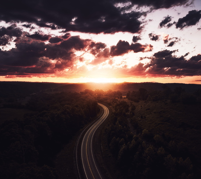 日落时树木环绕的道路鸟瞰图