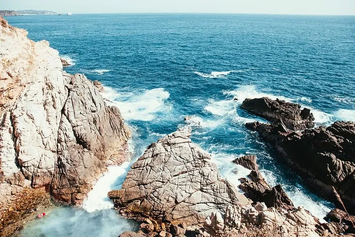 海边的天然岩石池，阳光下海浪拍打岩石