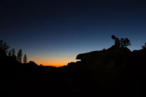 日落时分,美国约塞米蒂山谷一名男子坐在岩石上的剪影 日落时分,美国约塞米蒂山谷一名男子坐在岩石上的剪影
