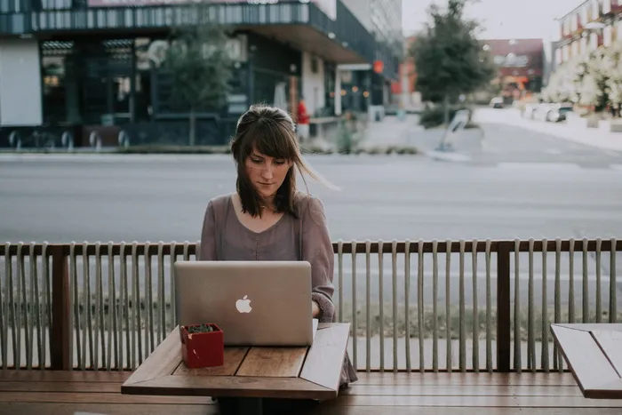穿着灰色衬衫的女人坐在MacBook前的长椅上