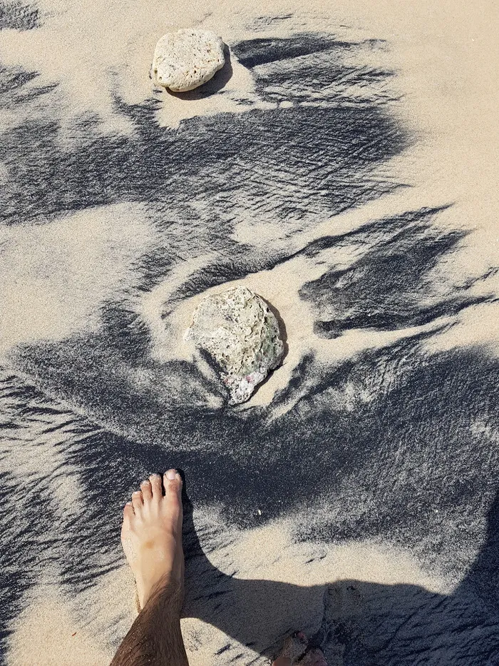 人的脚在岩石附近的沙子上