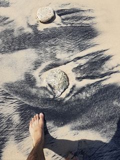 人的脚在岩石附近的沙子上