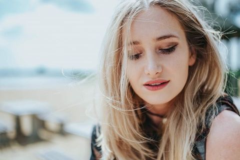 美丽的金发女人在海滩边的树桩上拿着一罐可乐放松