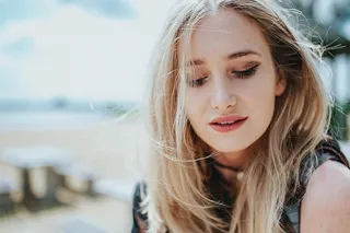 美丽的金发女人在海滩边的树桩上拿着一罐可乐放松