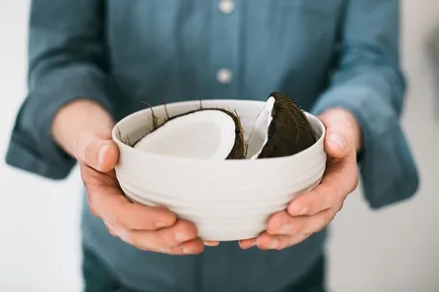 拿着白色陶瓷碗和一半椰子的人 拿着白色陶瓷碗和一半椰子的人