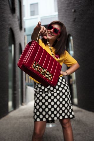 身穿黄色圆领T恤，手持红色手提包的女子