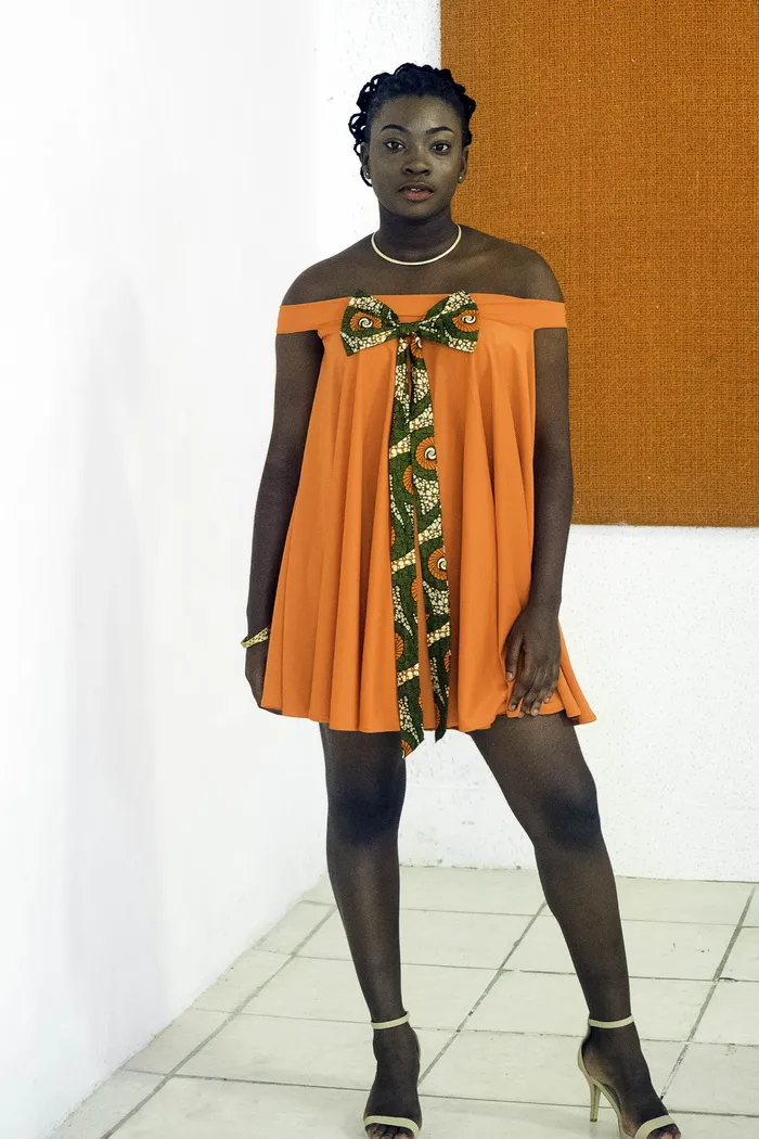 身着橙色露肩连衣裙的女子站在白墙附近的照片