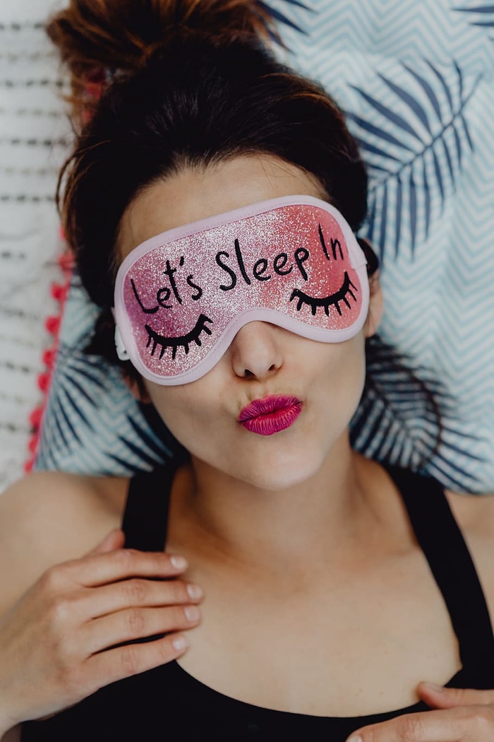 快乐女孩在卧室里放松-戴着粉色睡眠面罩的黑发女性俯视图