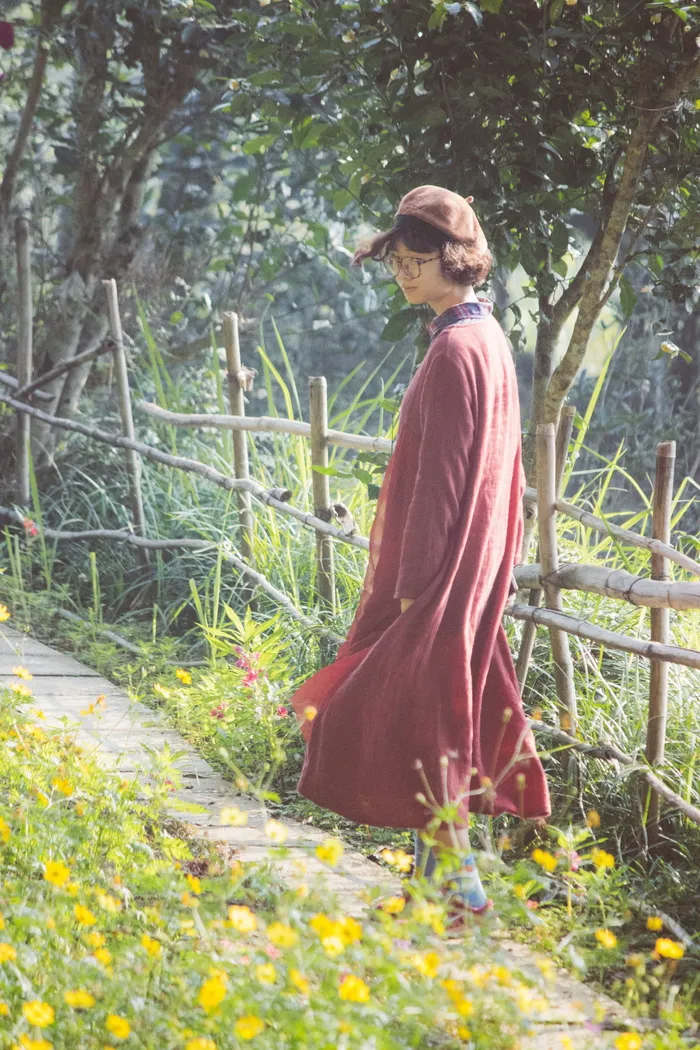 穿着红色长袍的女人走在花园的小路上