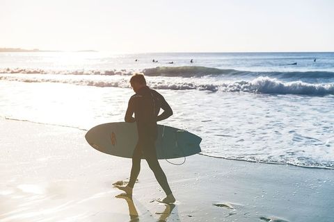 一名冲浪者在下海的路上走在海滩上，这张照片摄于英格兰康沃尔