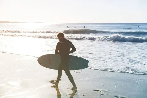 一名冲浪者在下海的路上走在海滩上，这张照片摄于英格兰康沃尔