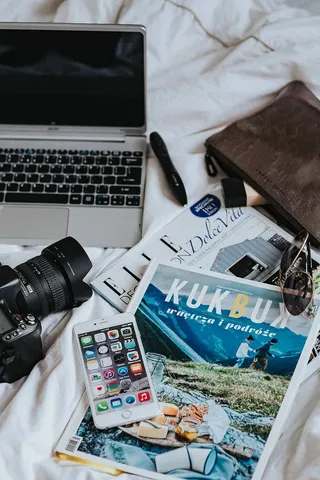 白色床单上的银色笔记本电脑、相机、杂志和其他物品