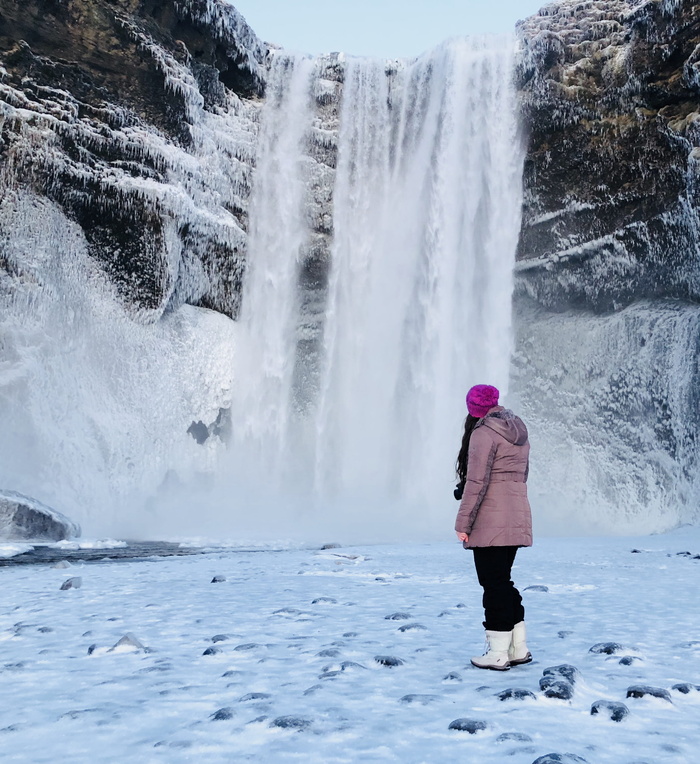 穿着粉色雪衣的女人站在结冰的瀑布前的雪地上