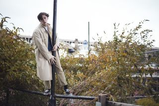 穿着米色派克大衣站在杆子上的男子