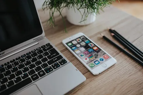 银色宏碁笔记本电脑放在一张木桌子上，上面有一株绿色植物、铅笔和一部苹果iPhone