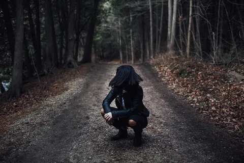白天,穿着黑色皮夹克的女人坐在树间的土路上 白天,穿着黑色皮夹克的女人坐在树间的土路上