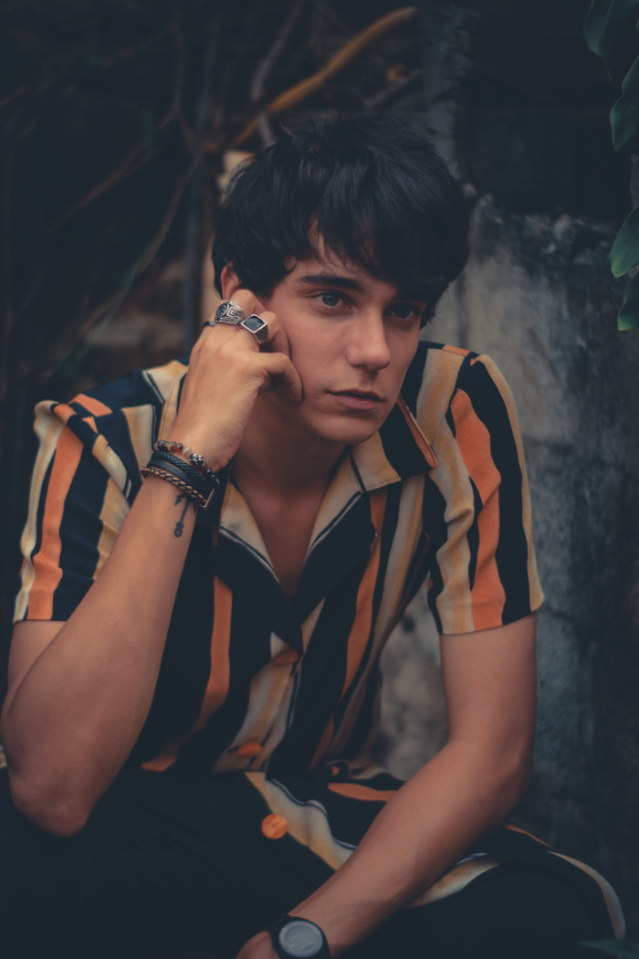 一名身穿五彩纽扣衬衫的男子坐在灰色混凝土墙附近