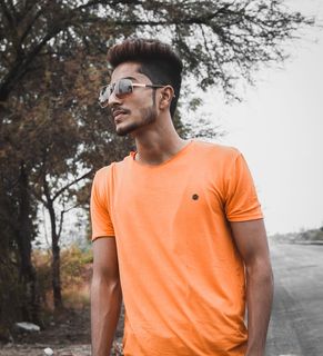 站在树旁穿着橙色圆领衬衫的男子