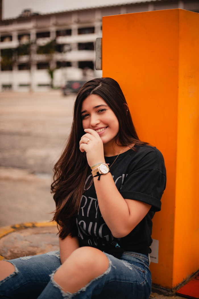 一位身穿黑色衬衫、面带微笑的女士坐在涂有橙色漆的柱子旁