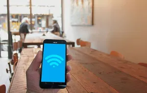 在城市的咖啡馆里，手持手机显示WiFi热点图标。